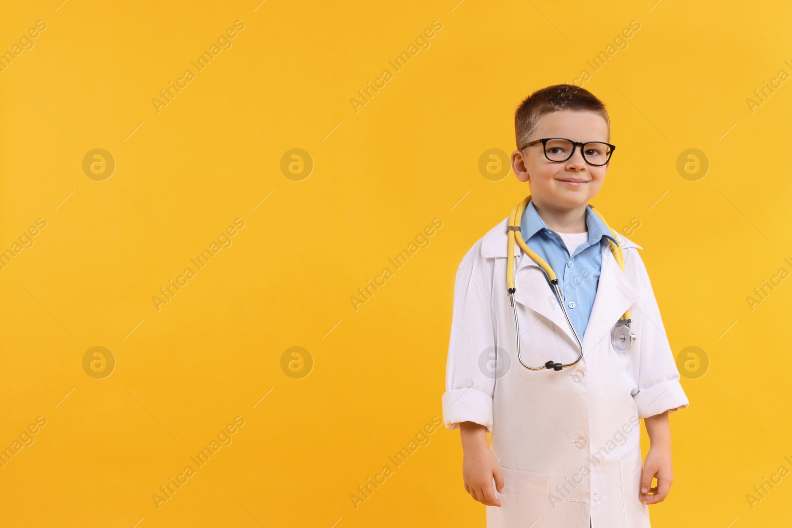 Photo of Little boy with stethoscope pretending to be doctor on yellow background, space for text. Dreaming of future profession