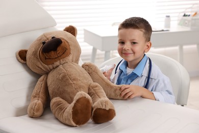 Photo of Little boy with stethoscope, syringe and toy pretending to be doctor indoors