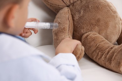 Little boy with stethoscope, syringe and toy pretending to be doctor indoors, closeup