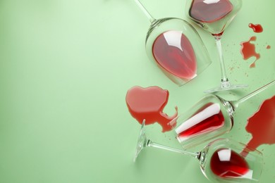 Photo of Glasses with spilled red wine on light green background, flat lay. Space for text