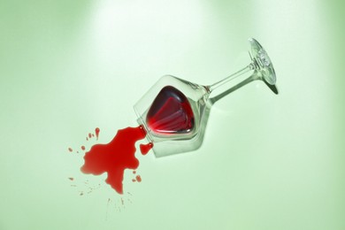 Photo of Glass with spilled red wine on light green background, top view