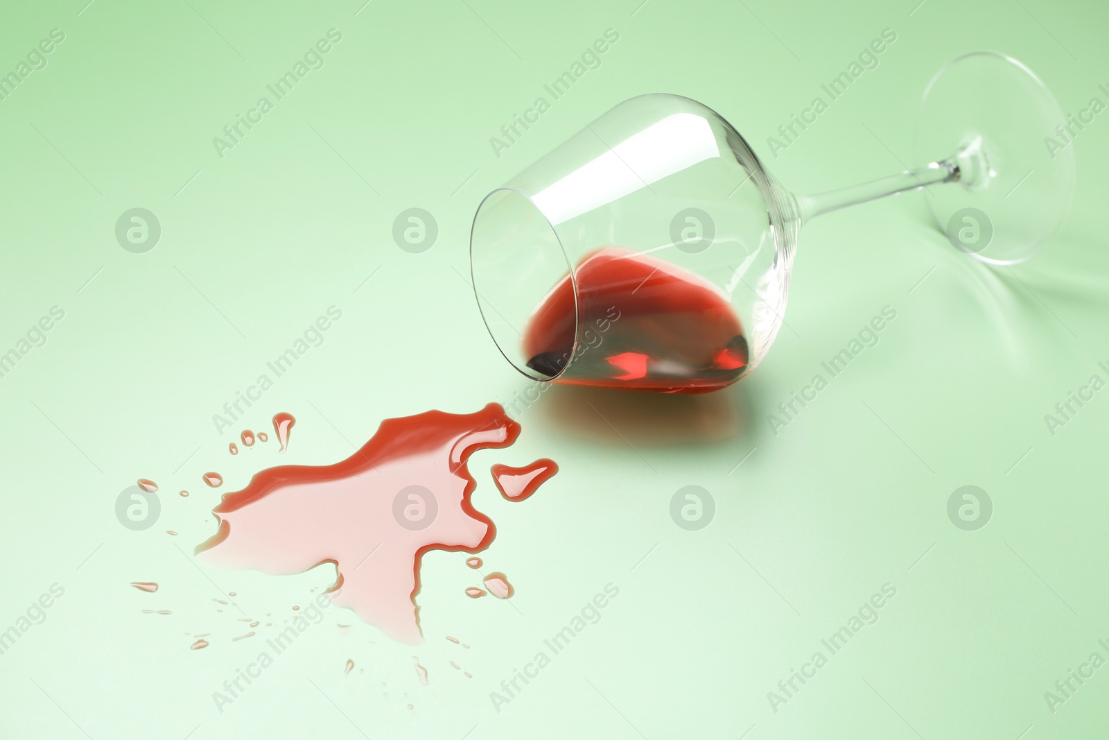 Photo of Glass with spilled red wine on light green background