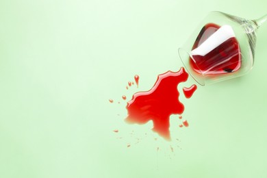 Photo of Glass with spilled red wine on light green background, top view. Space for text