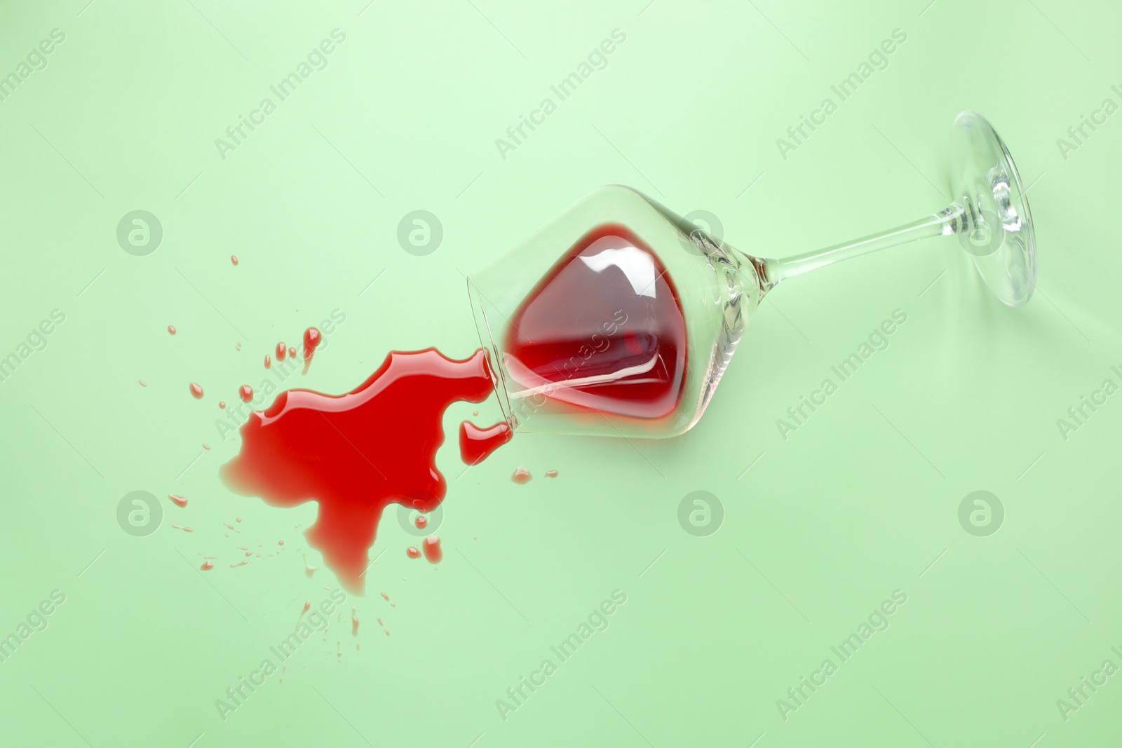 Photo of Glass with spilled red wine on light green background, top view