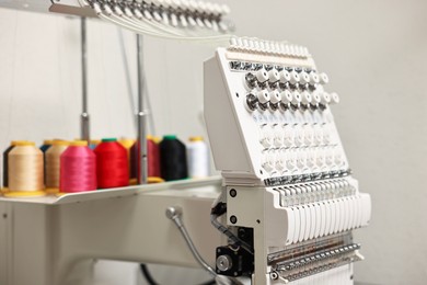 Photo of Modern embroidery machine with spools of thread indoors, closeup