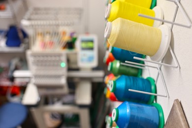 Photo of Spools of thread and modern embroidery machine indoors, selective focus