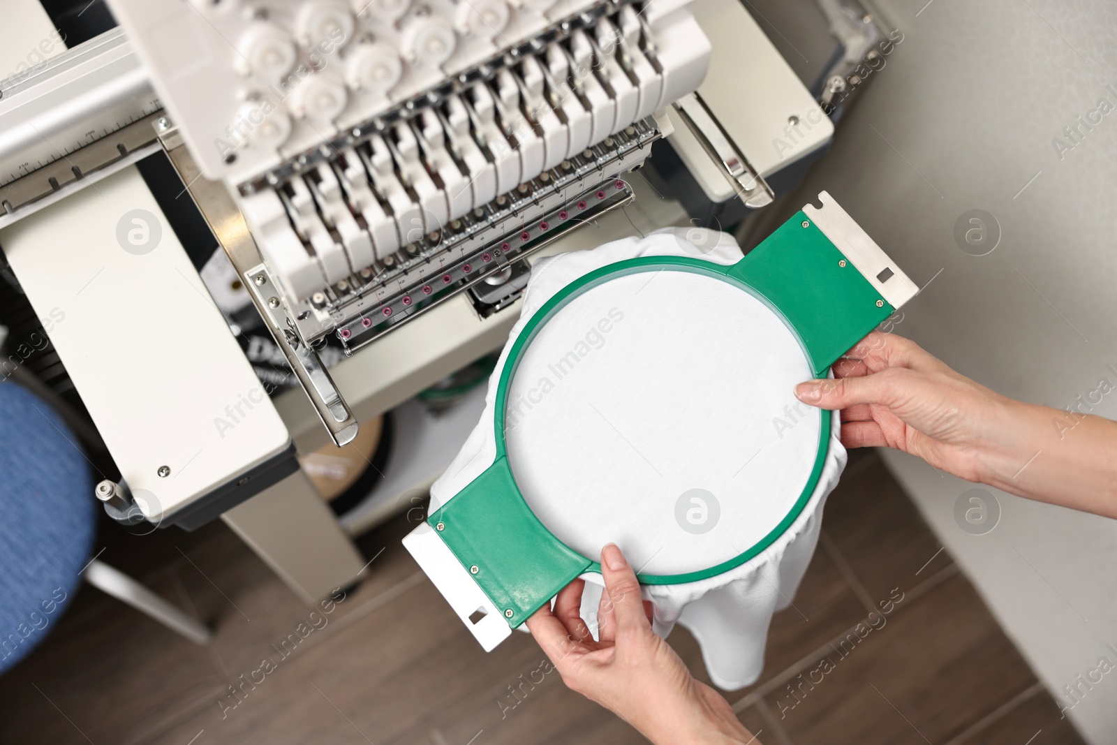 Photo of Woman using embroidery machine to make design on T-shirt indoors, closeup