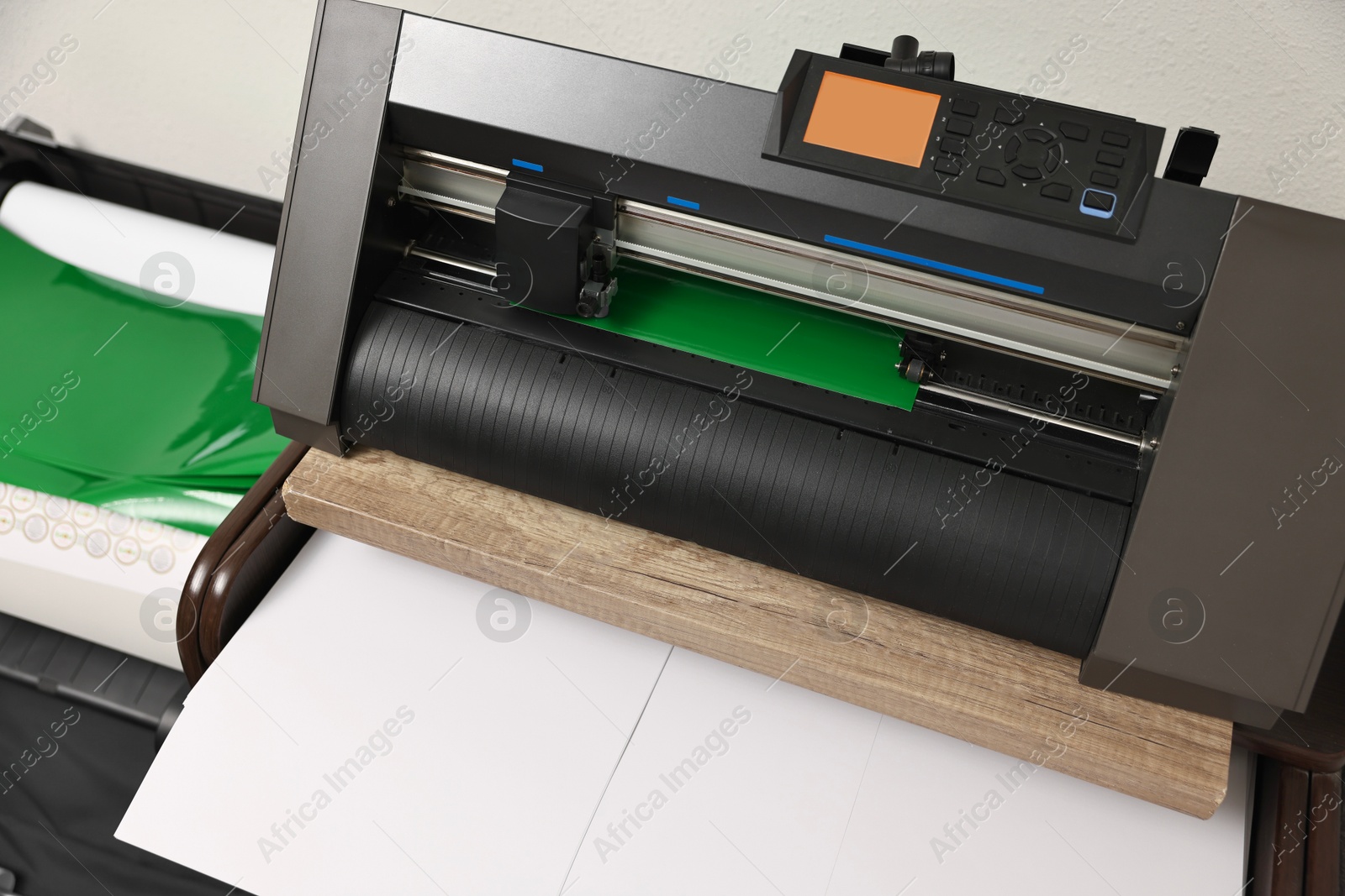 Photo of Modern cutting machine with green vinyl sheet indoors