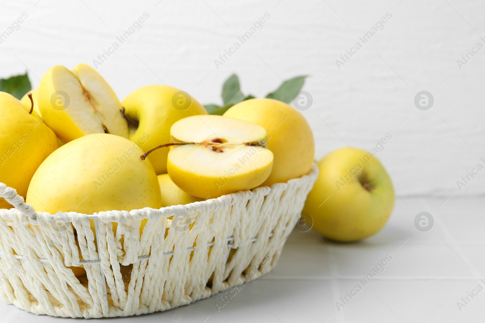 Photo of Fresh ripe yellow apples in basket on white tiled table, closeup. Space for text