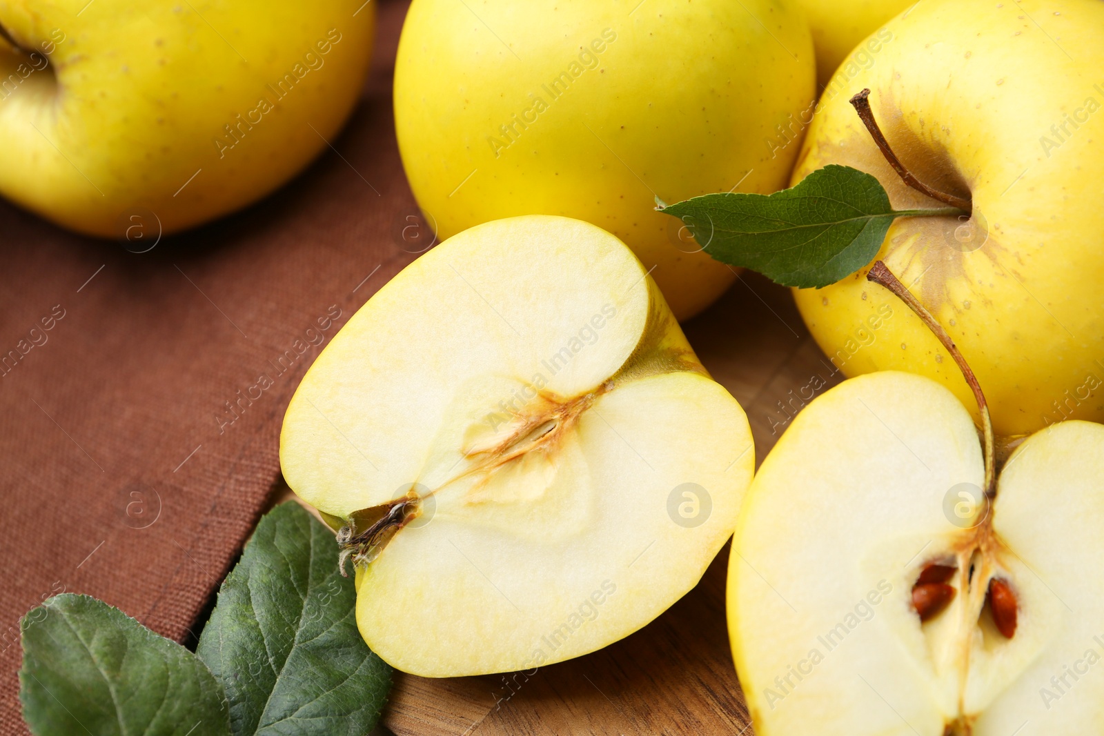 Photo of Fresh ripe yellow apples and green leaves on table, closeup