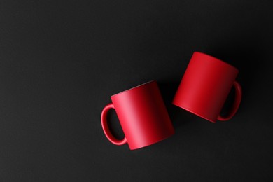 Photo of Two blank red mugs on black background, top view. Mockup for design