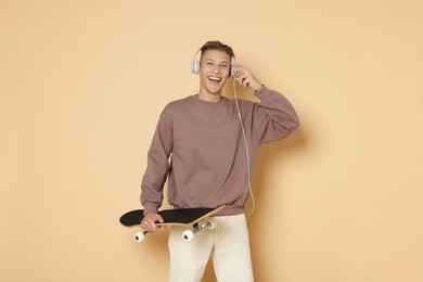 Happy man with skateboard and headphones on beige background