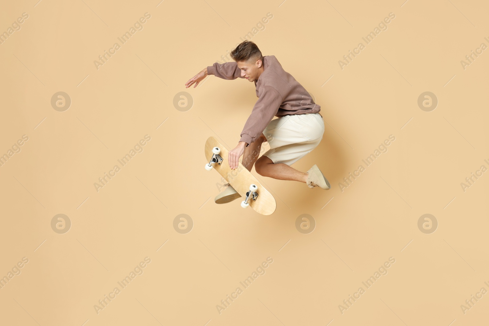 Photo of Handsome man jumping with skateboard on beige background