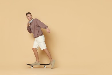 Happy man riding skateboard on beige background. Space for text