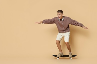 Happy man riding skateboard on beige background. Space for text