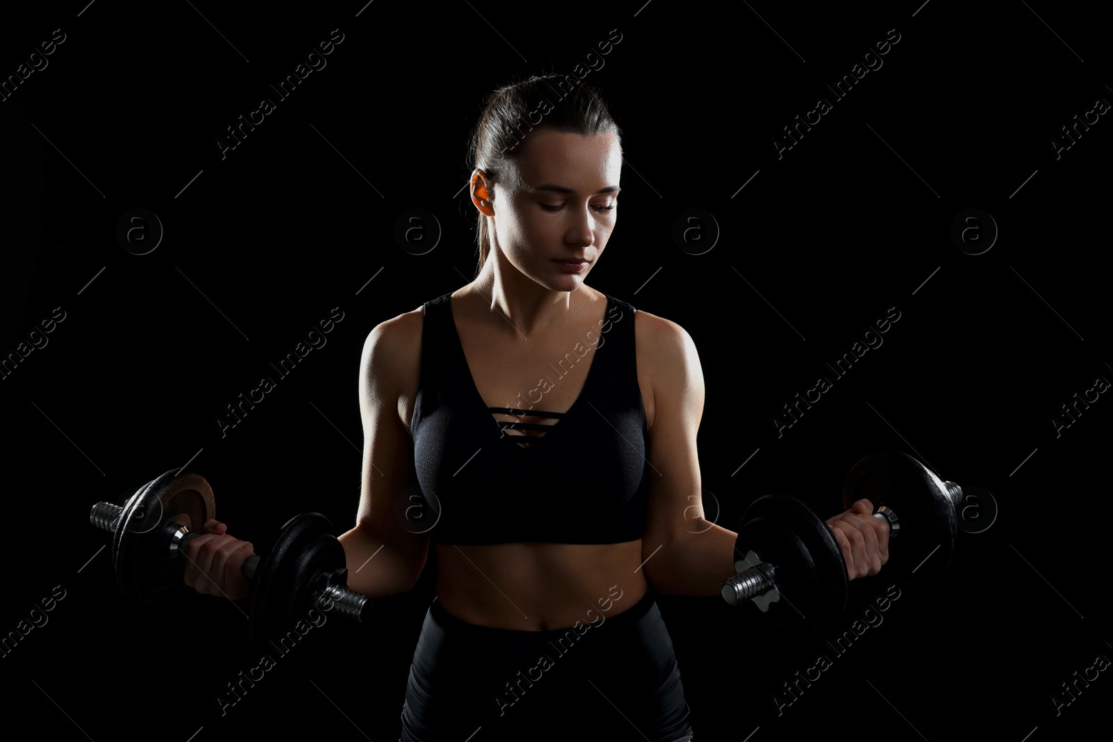 Photo of Beautiful woman in sportswear training with barbells on black background