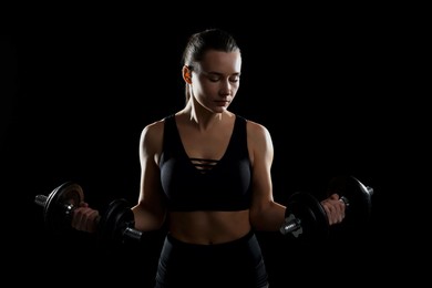 Photo of Beautiful woman in sportswear training with barbells on black background