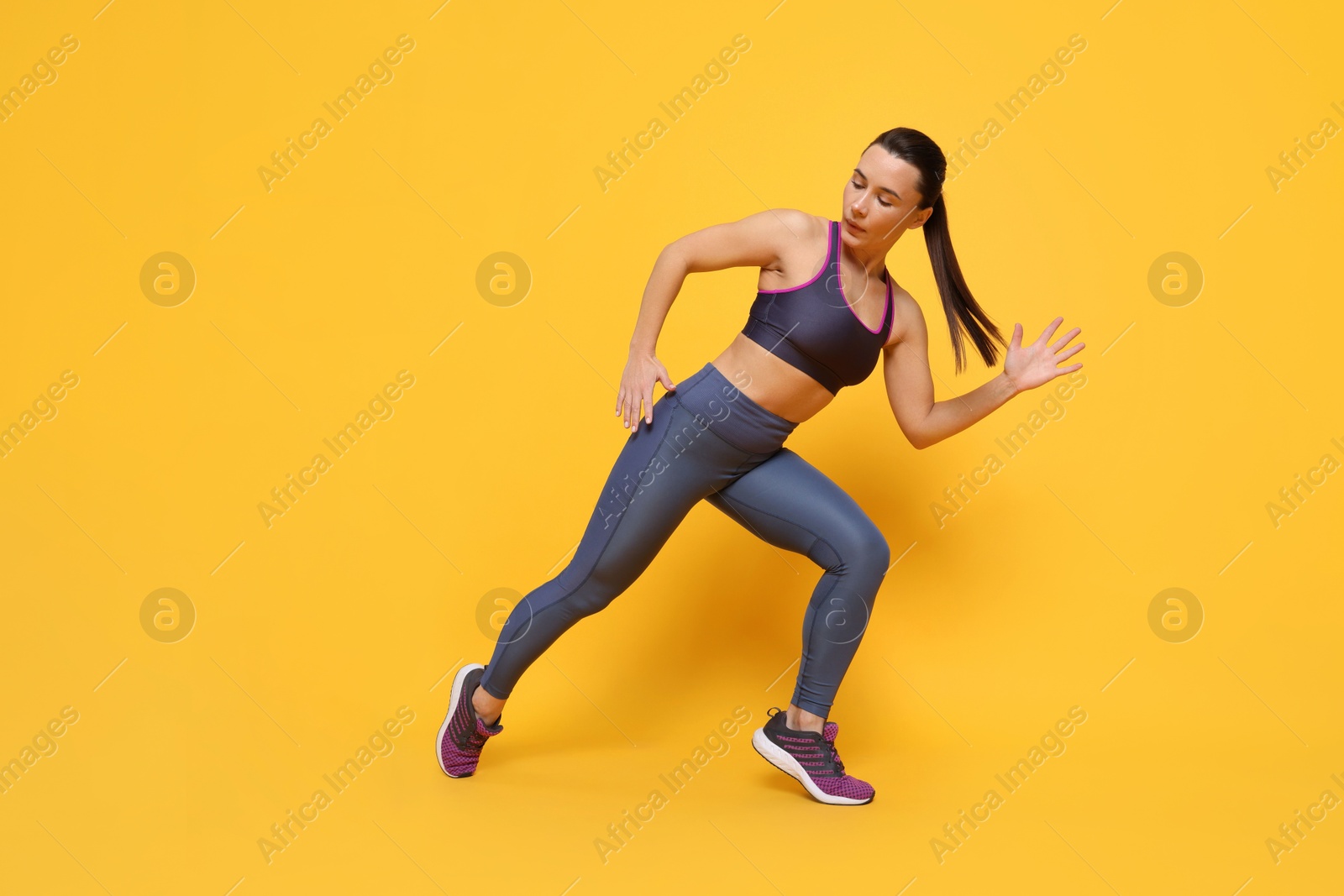 Photo of Beautiful woman in sportswear training on yellow background, low angle view. Space for text