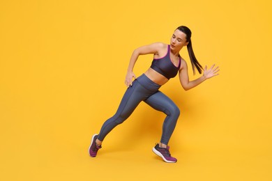 Beautiful woman in sportswear training on yellow background, low angle view. Space for text