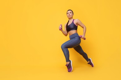 Beautiful woman in sportswear training with dumbbells on yellow background, low angle view. Space for text