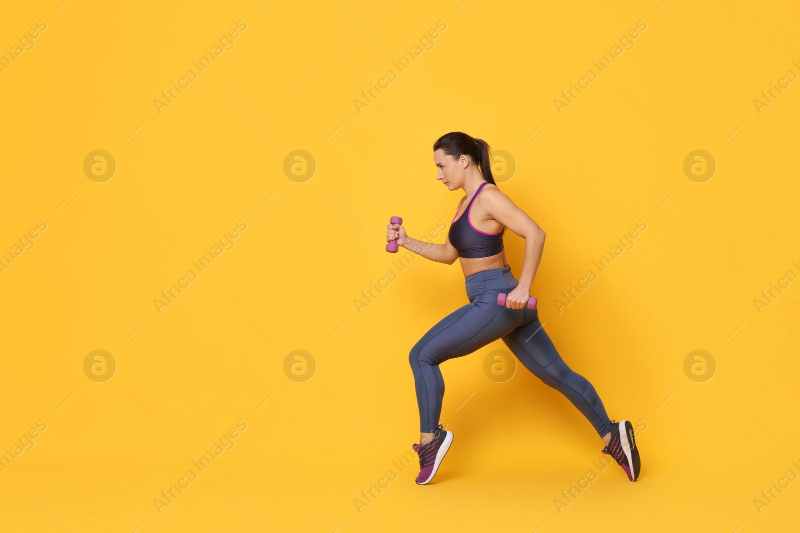 Photo of Beautiful woman in sportswear training with dumbbells on yellow background. Space for text