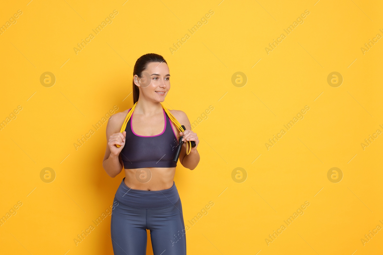 Photo of Smiling woman with skipping rope on yellow background. Space for text