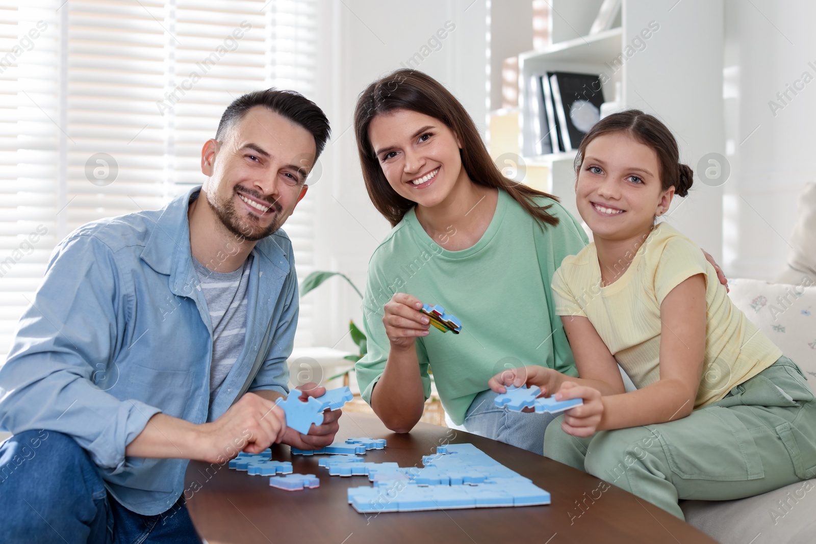 Photo of Happy parents and their daughter solving puzzle together at wooden table indoors