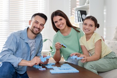 Happy parents and their daughter solving puzzle together at wooden table indoors