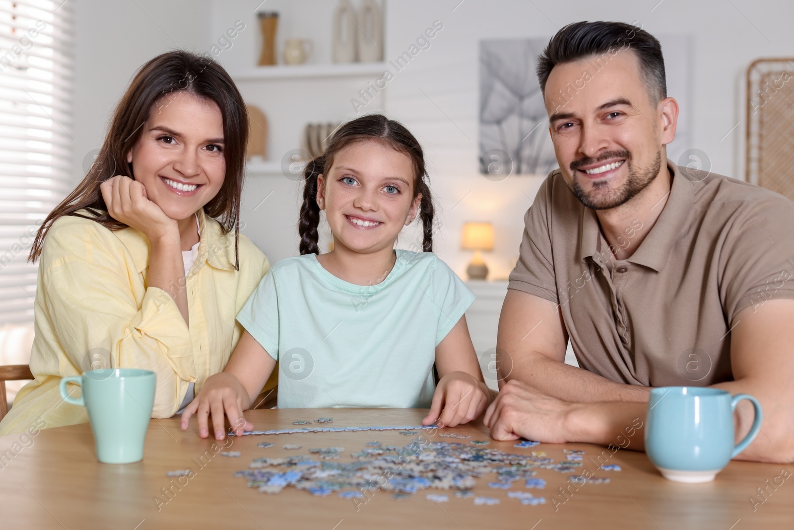 Photo of Happy parents and their daughter solving puzzle together at wooden table indoors