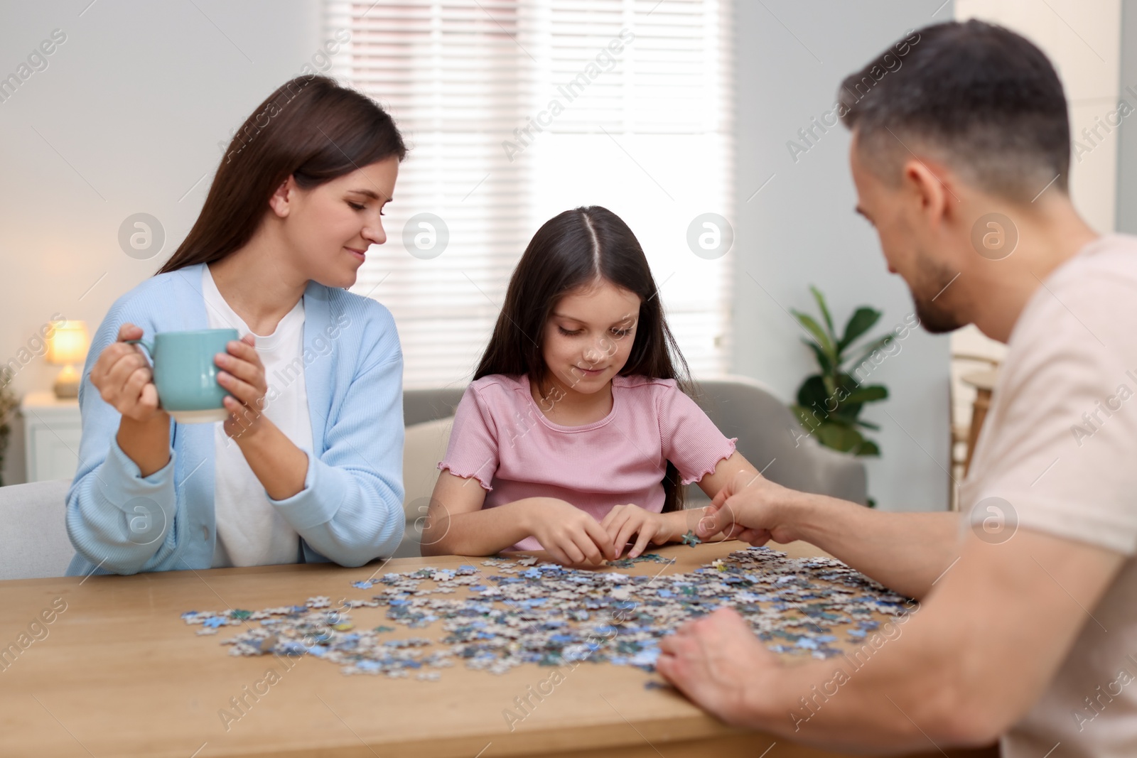 Photo of Happy parents and their daughter solving puzzle together at wooden table indoors