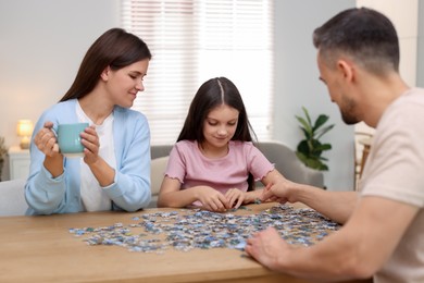 Happy parents and their daughter solving puzzle together at wooden table indoors