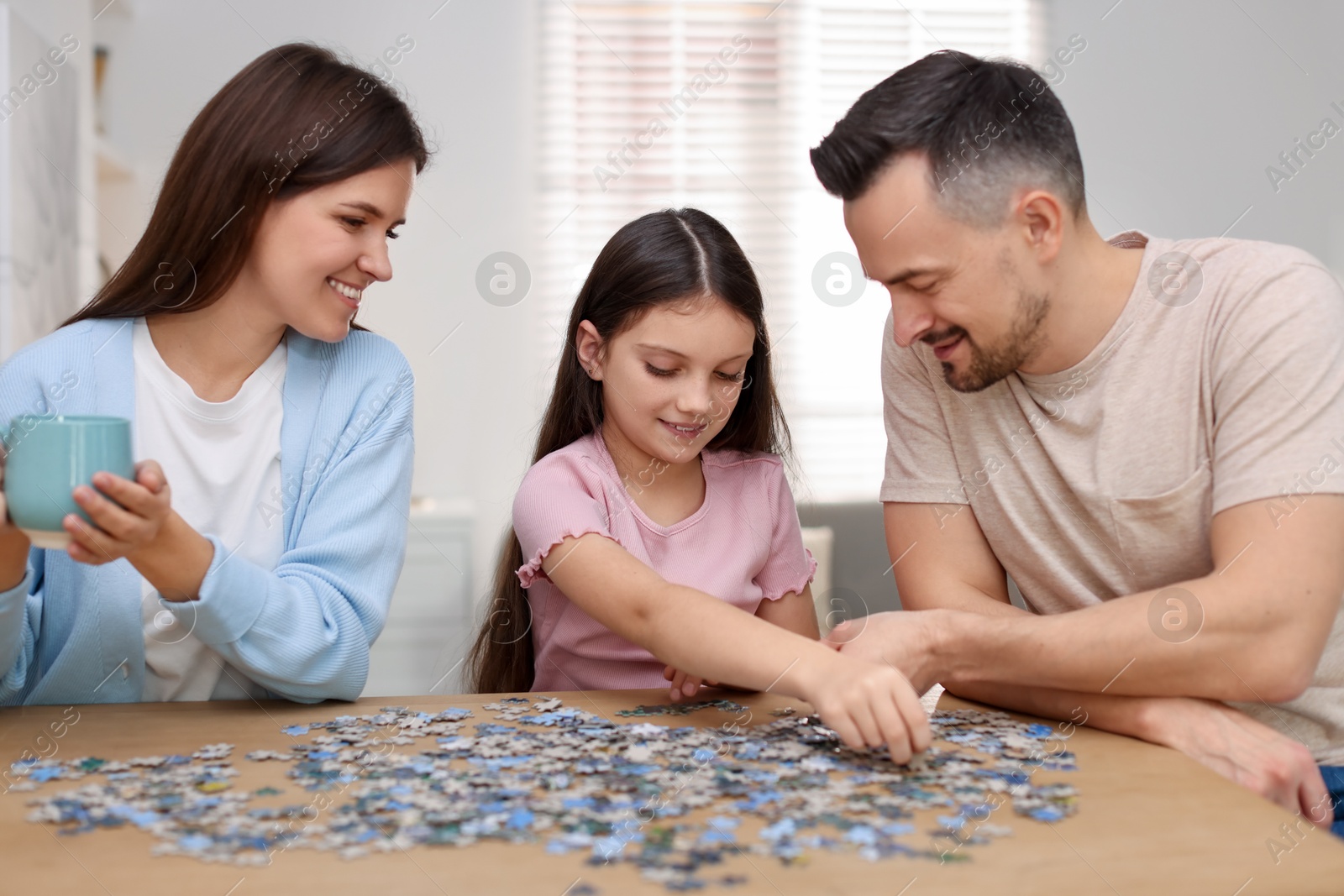 Photo of Happy parents and their daughter solving puzzle together at wooden table indoors