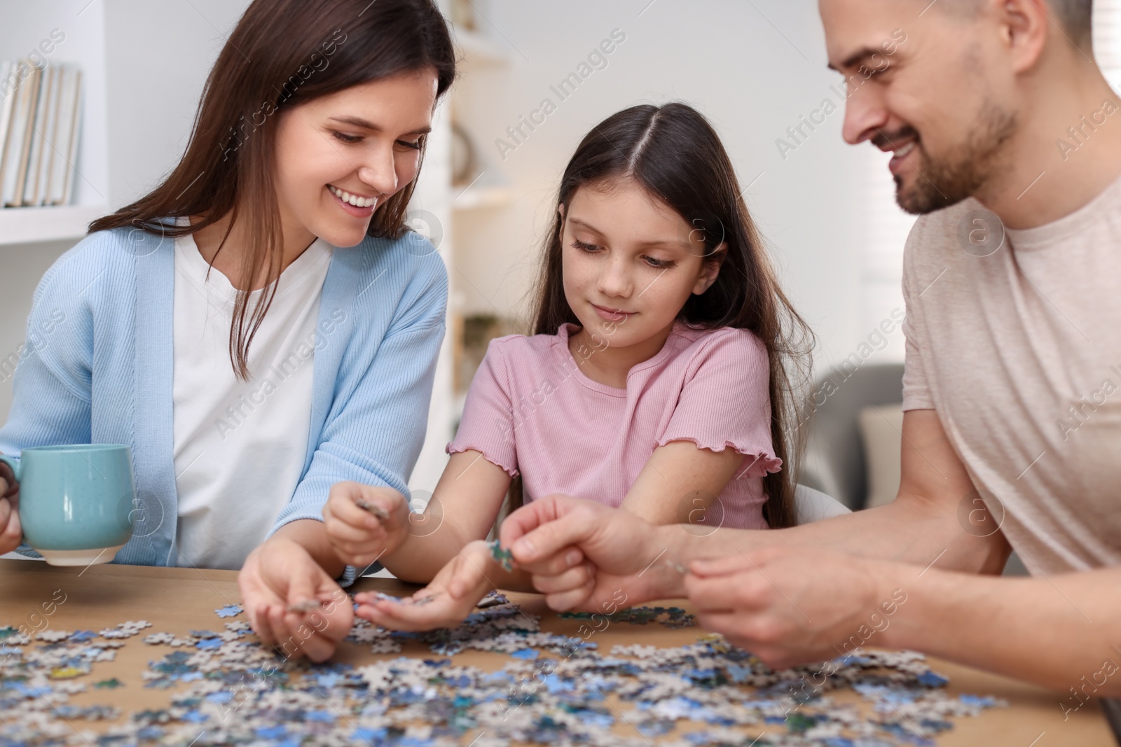 Photo of Happy parents and their daughter solving puzzle together at wooden table indoors