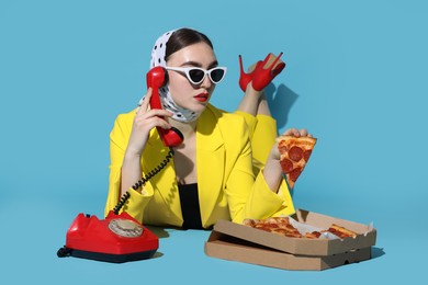 Stylish woman with delicious pizza and telephone on light blue background