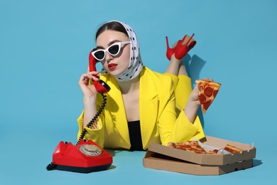 Stylish woman with delicious pizza and telephone on light blue background