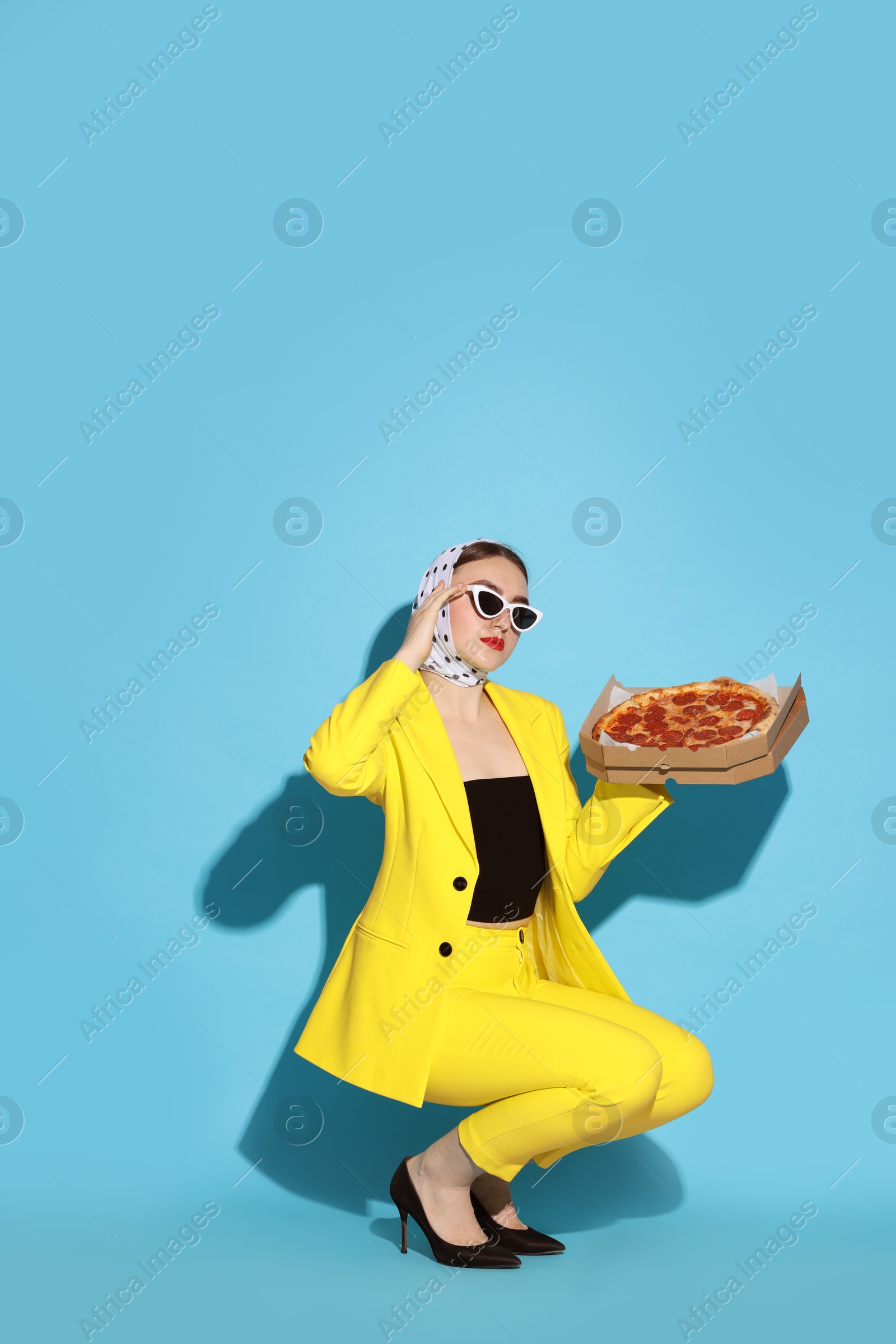 Photo of Stylish woman with delicious pizza on light blue background, space for text