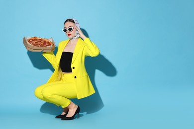 Photo of Stylish woman with delicious pizza on light blue background, space for text