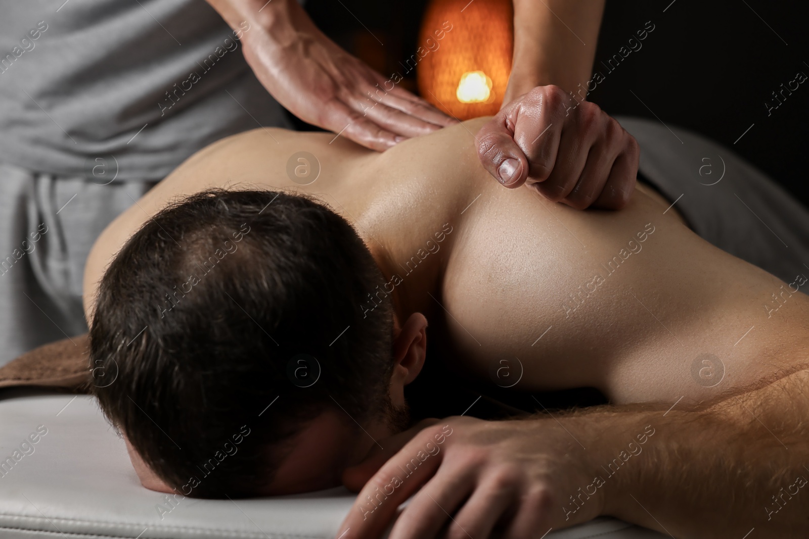 Photo of Professional physiotherapist doing shoulder massage for his client indoors, closeup