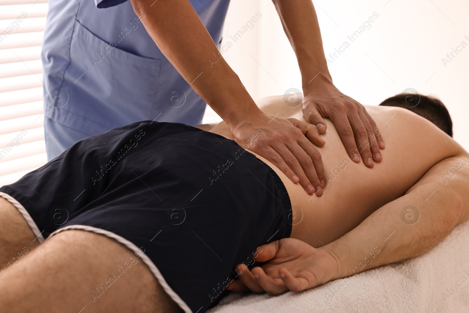 Photo of Professional physiotherapist doing back massage for his client indoors, closeup