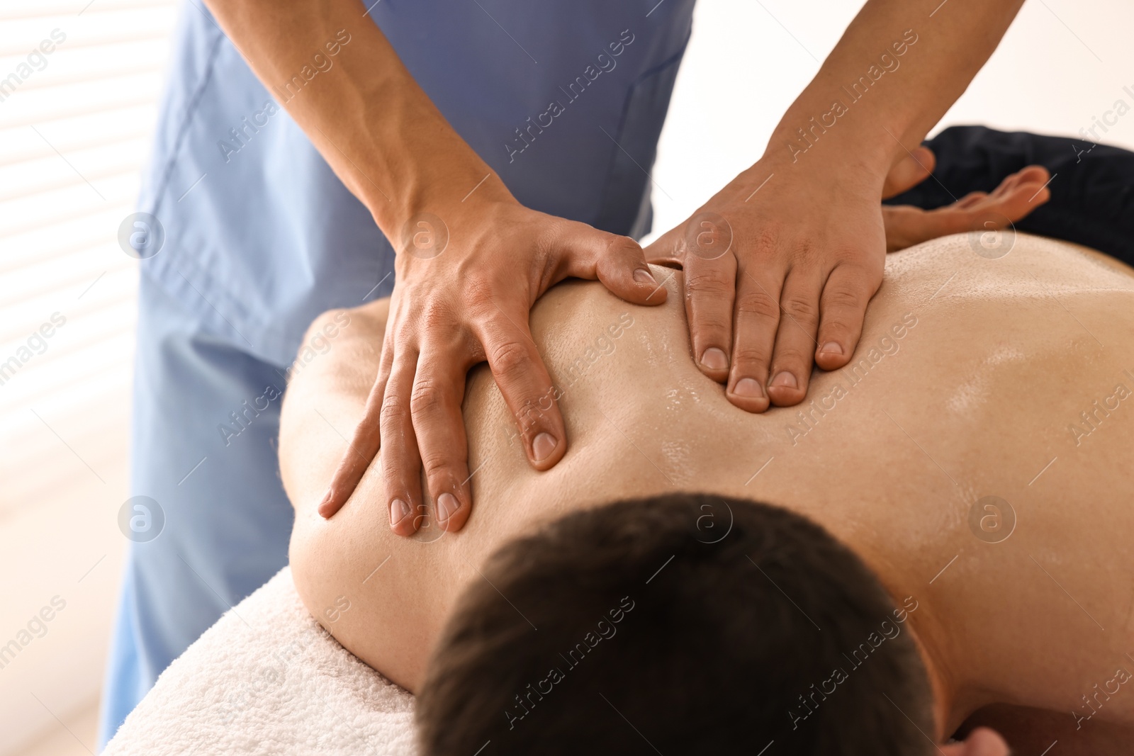 Photo of Professional physiotherapist doing shoulder massage for his client indoors, closeup