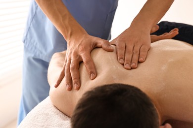 Photo of Professional physiotherapist doing shoulder massage for his client indoors, closeup