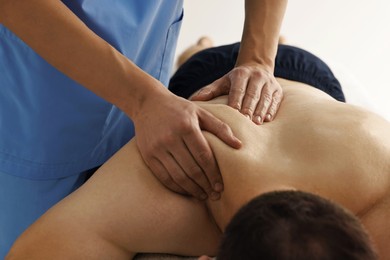 Photo of Professional physiotherapist doing shoulder massage for his client indoors, closeup