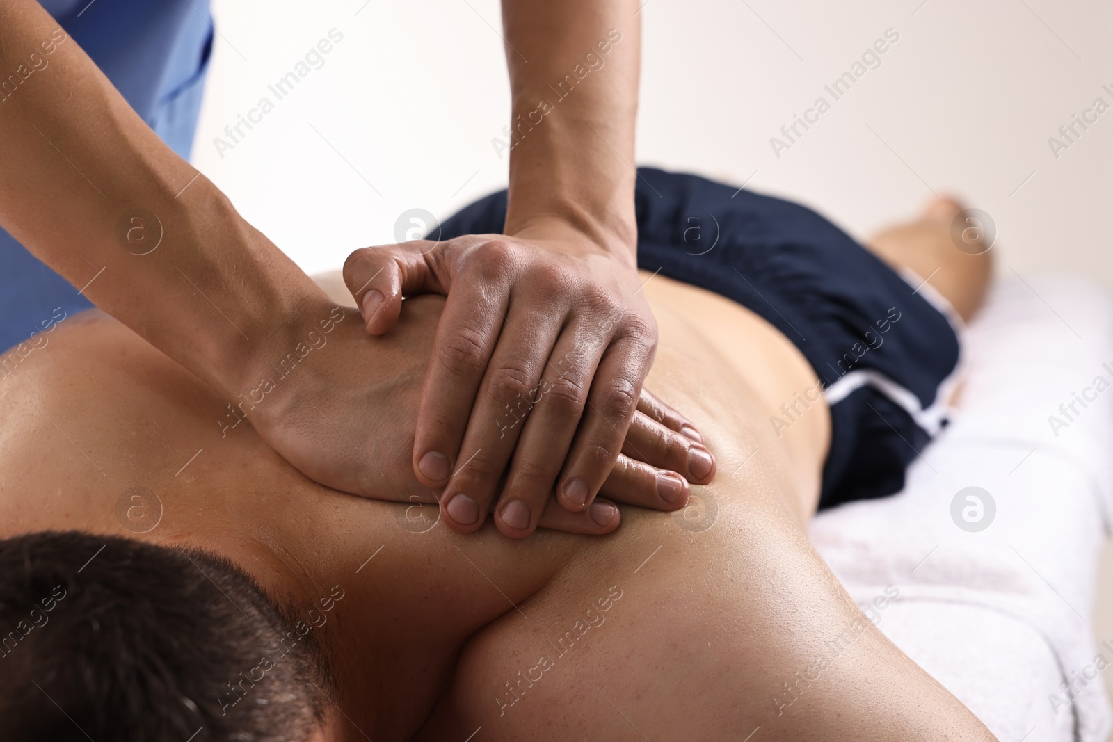 Photo of Professional physiotherapist doing shoulder massage for his client indoors, closeup