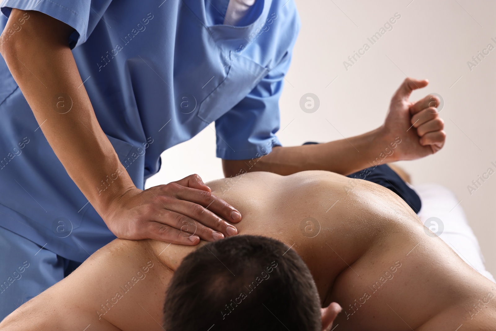 Photo of Professional physiotherapist doing back massage for his client indoors, closeup