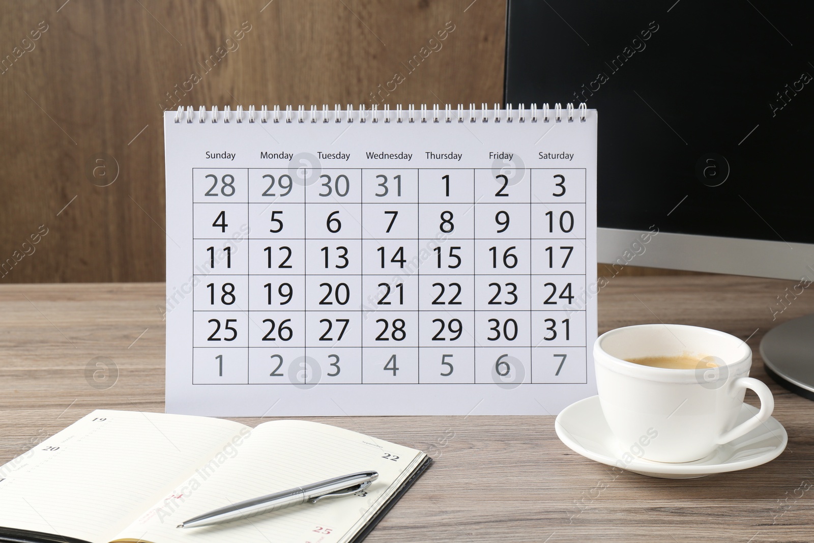 Photo of Timetable. Monthly planner, stationery, coffee and computer on wooden table