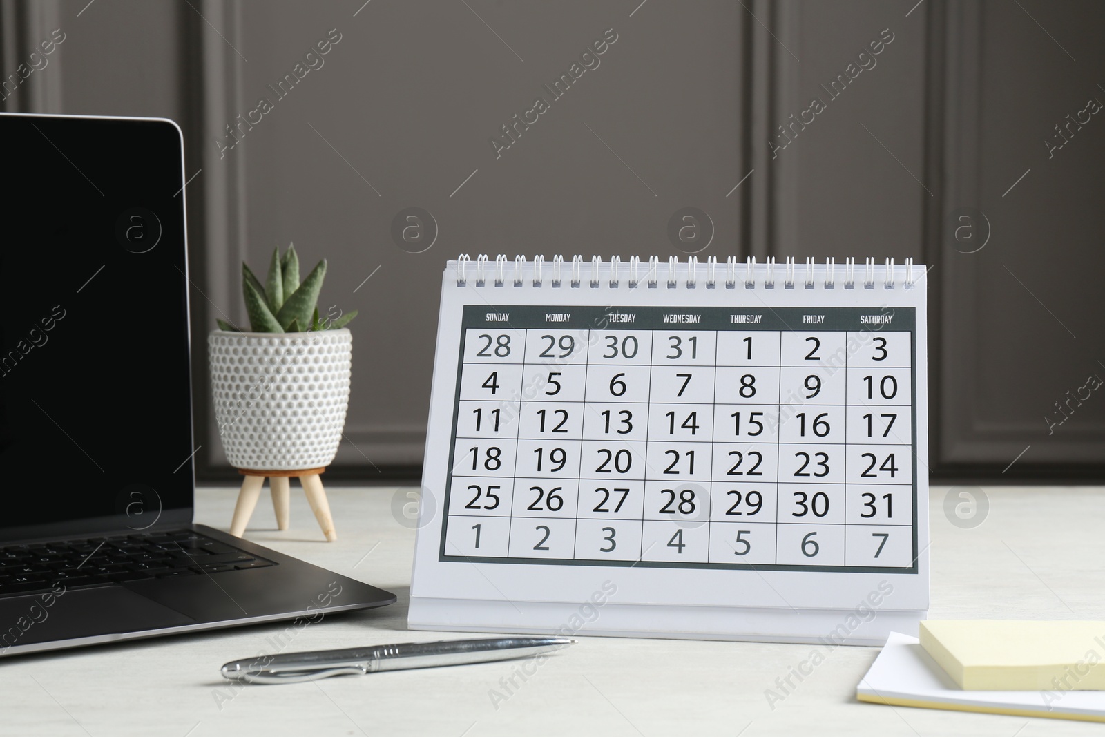 Photo of Timetable. Calendar, stationery, laptop and floral decor on white table