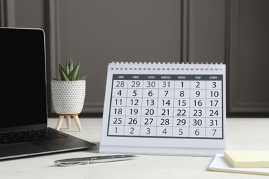 Photo of Timetable. Calendar, stationery, laptop and floral decor on white table