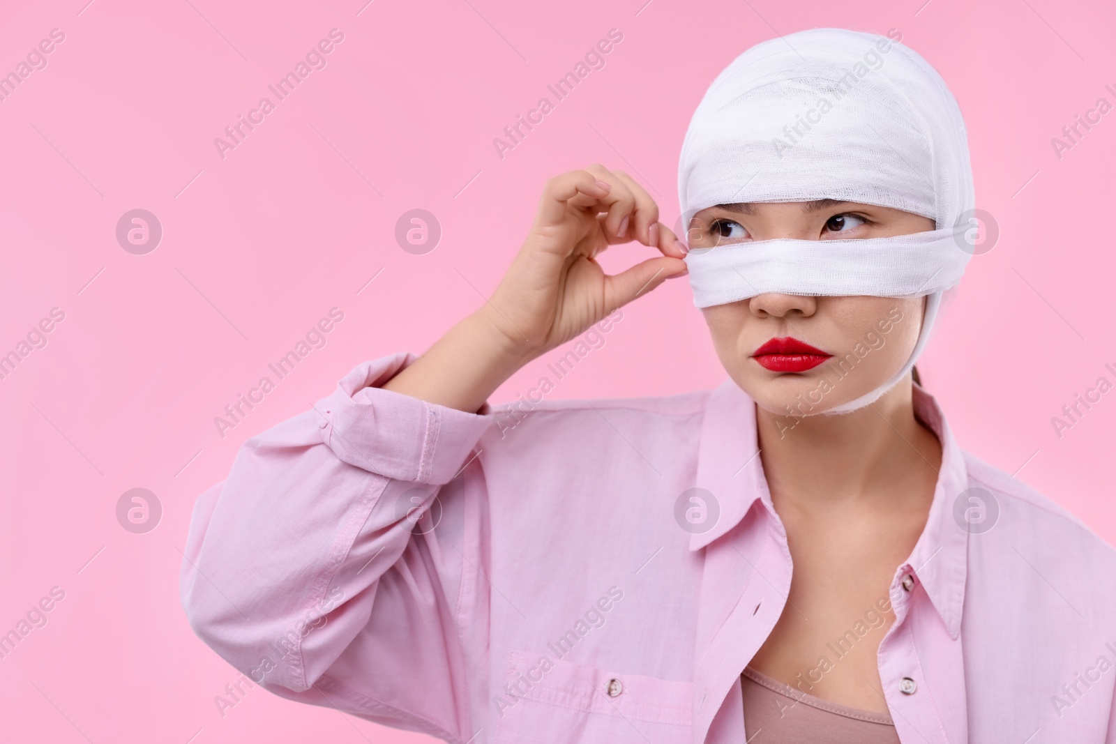 Photo of Woman with nose wrapped in medical bandage after plastic surgery operation on pink background