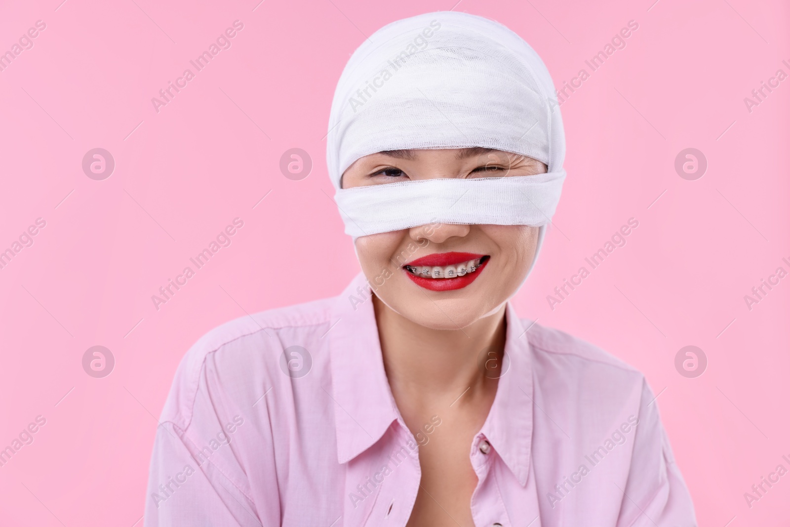 Photo of Woman with nose wrapped in medical bandage after plastic surgery operation on pink background