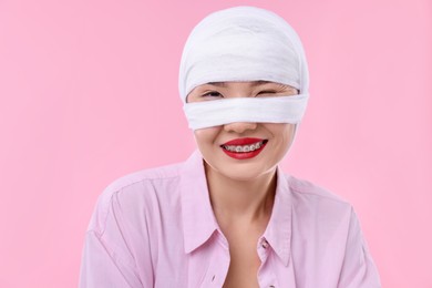 Woman with nose wrapped in medical bandage after plastic surgery operation on pink background